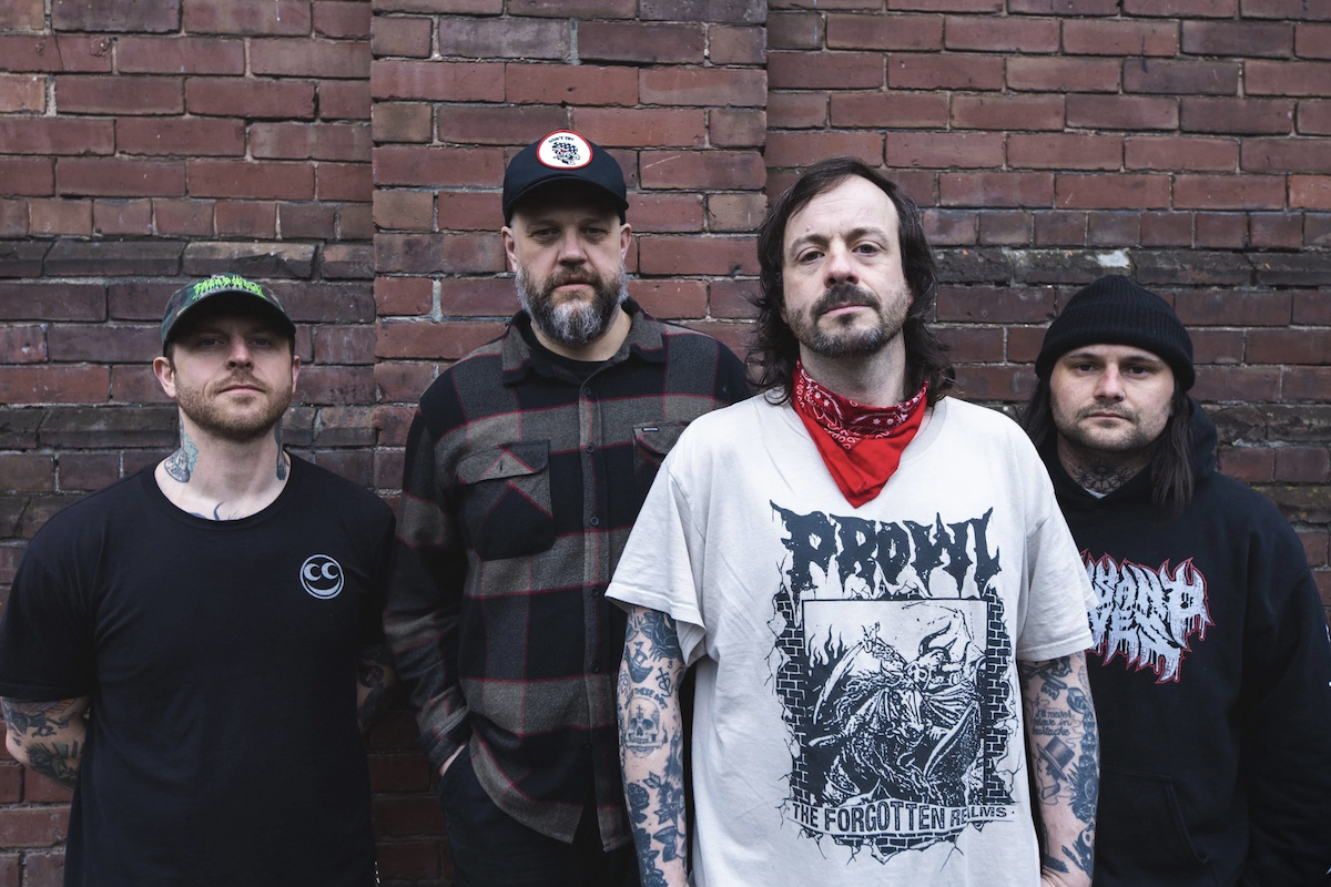 Canadian hardcore punk band Cancer Bats members posing together in front of a red brick wall, wearing casual band t-shirts and hats